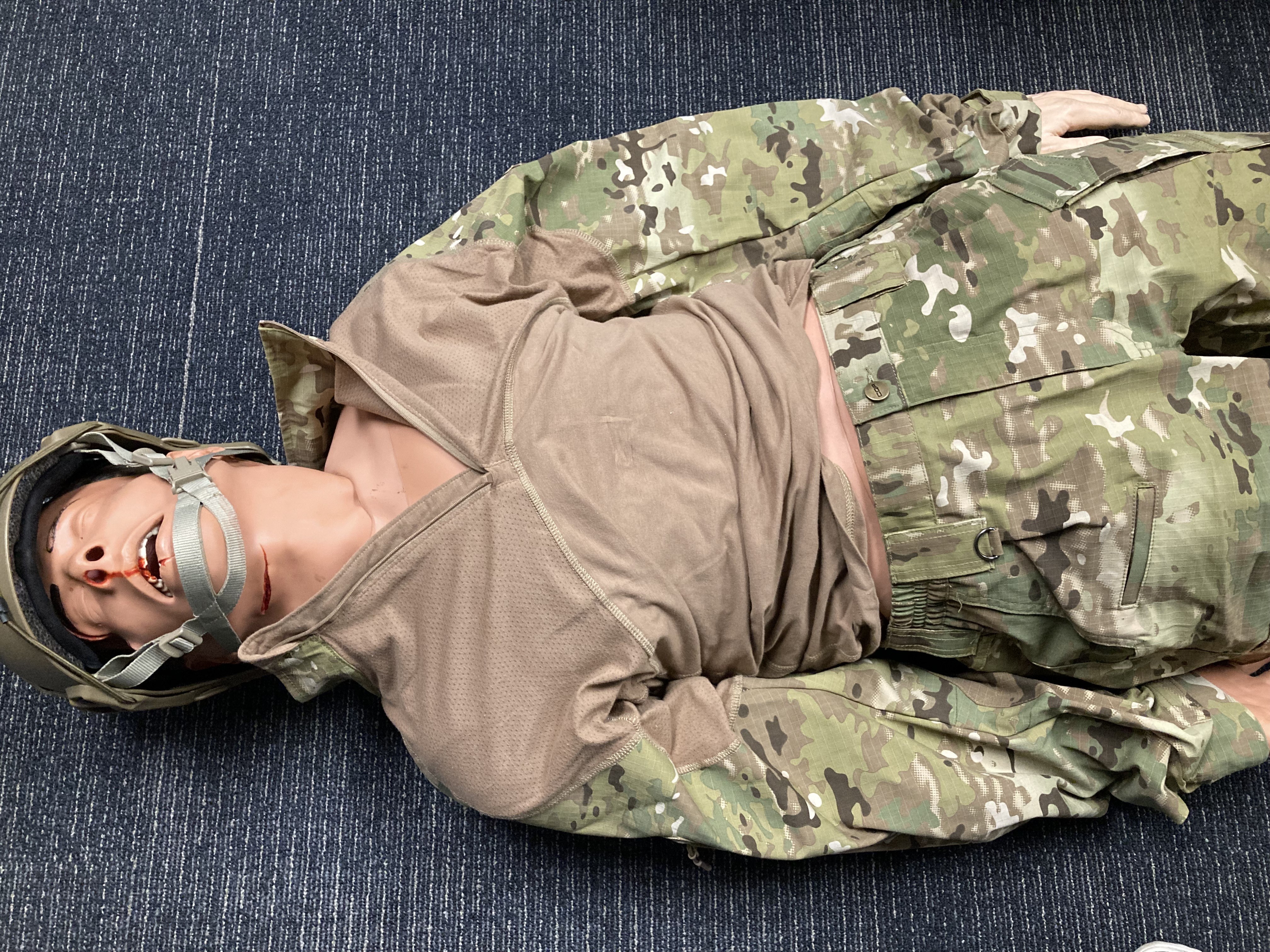 A patient simulator with a helmet, lying on the floor.